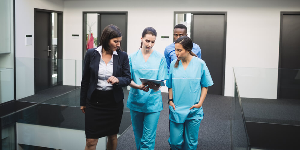 A nurse educator stands at the front of a classroom, in front of a group of nurses.