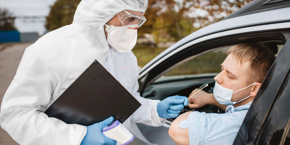 An NHS worker performing a COVID-19 nose swap test on a car passenger