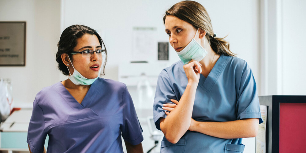 A smiling charge nurse in uniform holding a tab with patient records.