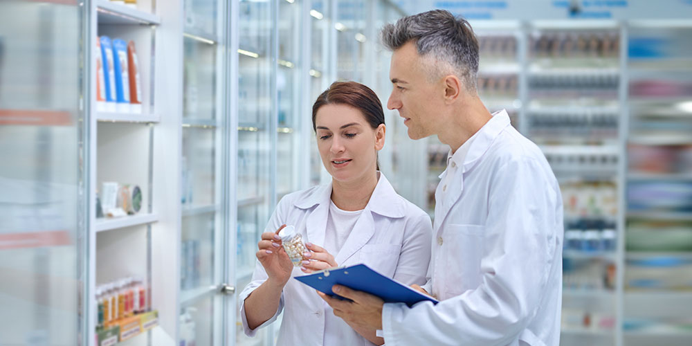 Two nurses converse and take notes about medications in the pharmacy.