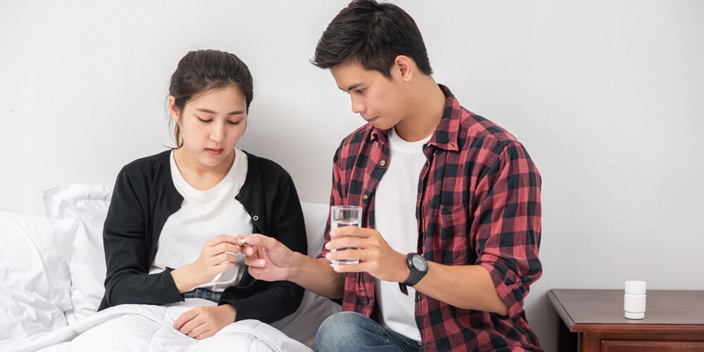 A young woman holding a pill and a glass of water, preparing to swallow it.