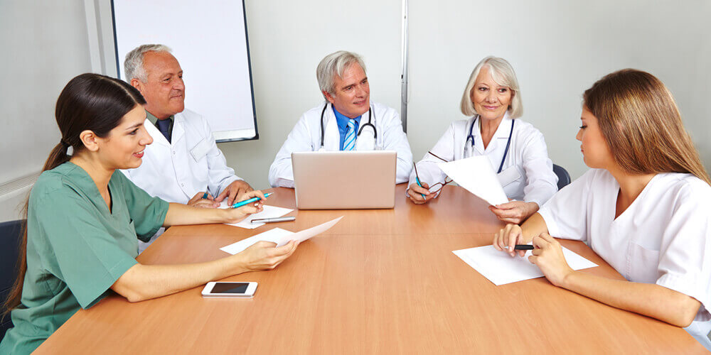 A nurse leader standing at the front of a board, addressing a group of staff members.