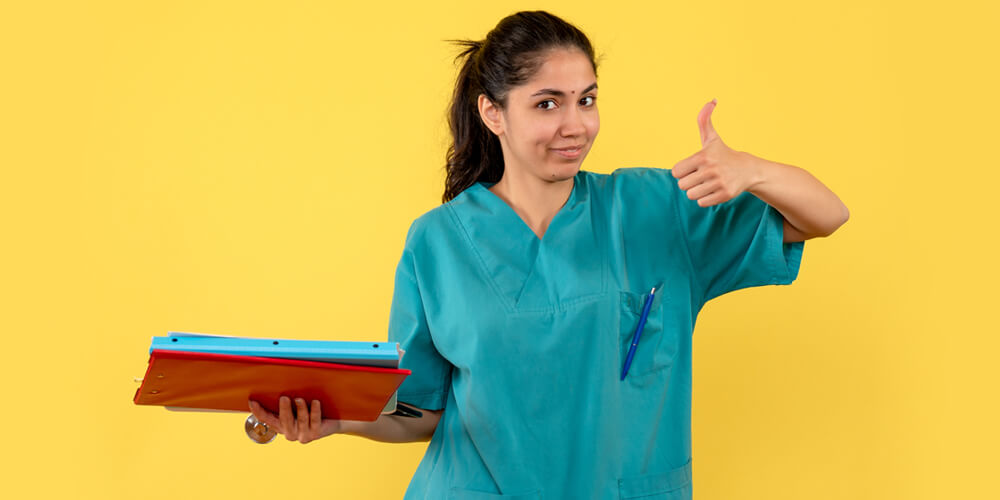 A nursing staff member poses for a photo while holding a grey laptop.