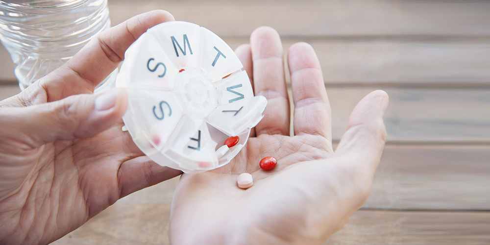 A person administering medication with the help of a pill organiser.