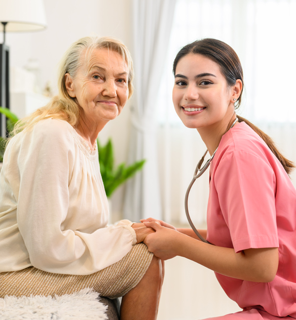 A healthcare worker and an elderly woman sitting and holding hands.